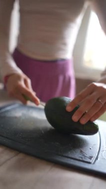 Yakından çekilmiş bir fotoğraf. Avokadoyu ustalıkla dilimliyor. Saf, siyah bir kesme tahtasının üzerinde.