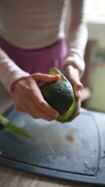 Parlak ve modern bir mutfakta mükemmel olgunlaşmış bir avokadoyu nazikçe sıkan bir el sağlıklı bir yemek hazırlığına hazırlanıyor.