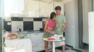 Neşeli bir çift, taze ve canlı malzemelerle dolu parlak bir mutfakta birlikte yemek pişiriyor.