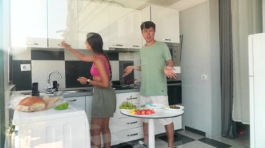Neşeli bir çift, taze ve renkli malzemelerle dolu parlak ve rahat bir mutfakta birlikte yemek pişirmekten zevk alır.