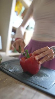 Yetenekli bir insan ahşap bir tahtanın üzerinde canlı kırmızı bir dolma biber kesiyor. Mutfak aromayla dolu.