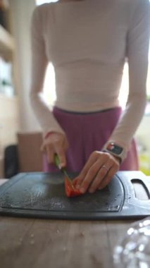 Yetenekli bir insan, mükemmel olgunlukta ve sulu bir domatesi rahat bir mutfakta ahşap bir kesme tahtasıyla ustalıkla dilimliyor.