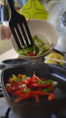 Canlı, yakışıklı bir aşçılık sahnesi. Kırmızı dolmalık biberler ve sıcak tavada cızırdayan taze yeşil soğanlar.