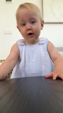 Açık mavi gözlü meraklı bir bebek yan bakıyor, masumiyeti keşfediyor, karanlık bir masaya dokunuyor. Güzel an