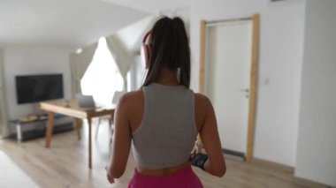 Kulaklık takan genç bir kadın, müzik deneyimine tamamen dalmış, modern ve parlak bir odada bulunur.