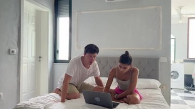 Bir çift aktif olarak birlikte bir dizüstü bilgisayar üzerinde çalışıyorlar. Parlak, modern, samimi ve davetkar bir yatak odası ortamında.