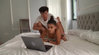 Genç bir çift şık yatak odalarında dizüstü bilgisayar üzerinde çalışırken rahat ve samimi bir anın tadını çıkarıyor.
