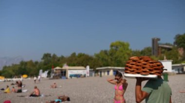 Neşeli güneşlenenlerle dolu hareketli ve canlı bir sahil sahnesi ve lezzetli atıştırmalıklar taşıyan bir yiyecek satıcısı.