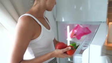Modern bir buzdolabından taze sebze seçen bir insan sağlıklı yaşam ve beslenmeyi kucaklıyor.