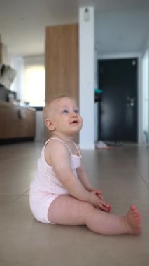 Sevimli küçük bir bebek renkli fayanslarla döşenmiş bir zeminde, modern ve şık bir mutfak düzeniyle mutlu bir şekilde oturuyor.