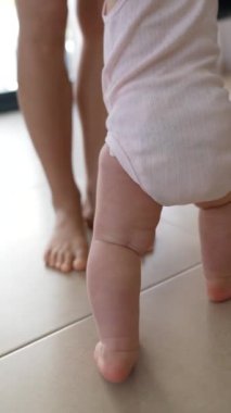 Bir çocuk, arka planda ebeveyniyle fayans zemininde yürümeye başlar, erken çocukluk dönüm noktalarını vurgular