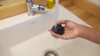 Bir el, mutfak lavabosunun akan suyunda pürüzsüz bir taş tutar. Temizlik ve doğada güzelliği ön plana çıkarır.