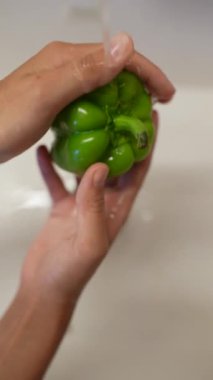 Bir el yeşil bir dolma biberi tutar, iyi hijyen uygulamalarının takip edildiğinden emin olmak için suyun altında durulatır.