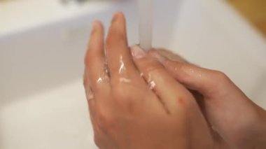 İyi aydınlatılmış bir mutfak ortamında akan suyun altında canlı yeşil bir dolma biberi dikkatlice temizleyen bir el.