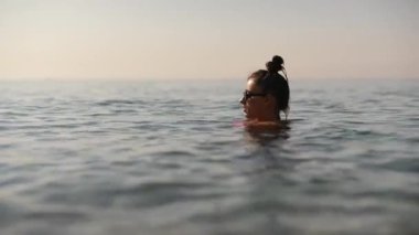 Şok edici bir günbatımında yumuşak dalgalarda süzülen ve saf sükuneti yakalayan bir bireyin huzurlu görüntüsü.