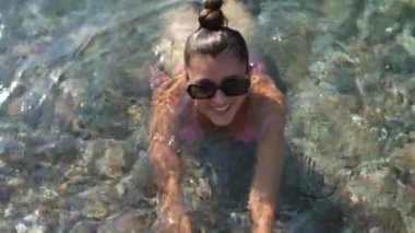 Sıcak bir yaz gününün özünü yakalayan, kristal berrak suda neşeyle yüzen bir kadının çarpıcı bir görüntüsü.