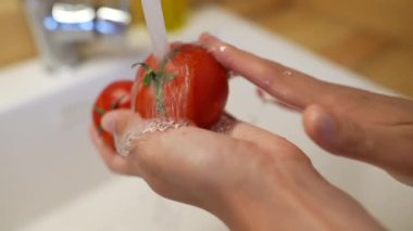 Eller taze ve olgun domatesleri mutfak lavabosunda dikkatlice yıkıyor ve lezzetli yemek pişirme seanslarına hazırlanıyor.