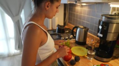 Genç bir kadın rengarenk bir mutfakta taze sebzeleri ustalıkla dilimleyip sağlıklı yemek yapma tutkusunu sergiliyor.