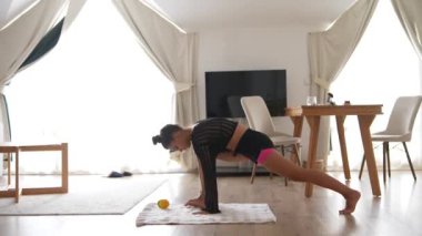 Evde yoga pozu veren zarif bir kadın şık ve sıcak bir iç mekanda zindelik ve sağlığını yansıtıyor.