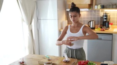 Genç bir kadın, parlak ve modern bir mutfak ortamında lezzetli yemekler hazırlama sürecine dikkatle odaklanır.