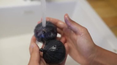 Bir kişi lavaboda akan suyun altında özenle taze bir meyveyi yıkıyor ve gıda hijyeninin önemini vurguluyor.