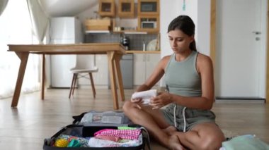 Genç bir kadın şık ve modern bir apartman dairesinde rahatça otururken bavulunu düzenliyor.