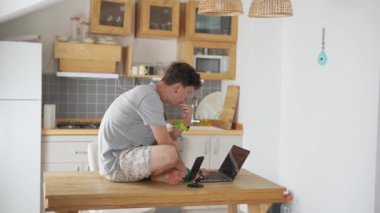 Odaklanmış bir birey, modern bir mutfakta, uzak çalışma eğilimlerini vurgulayarak, parlak bir dizüstü bilgisayar üzerinde verimli bir şekilde çalışır.