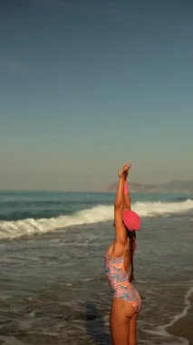 Neşeli ve enerjik bir figür, okyanus dalgalarının tadını çıkarırken, sıcak güneşin tadını çıkararak kıyı şeridinde duruyor.