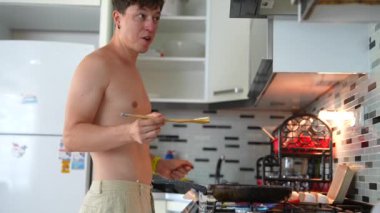 Üstsüz bir adam modern bir mutfakta yemek pişiriyor, yaratıcılığının rahatlamış bir anını özenle sergiliyor.