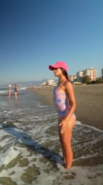 Neşeli bir çocuk, güneşli ve davetkar bir sahilde, dalgaların arasında mutlu bir şekilde duruyor.