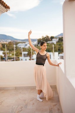 Yetenekli bir dansçı büyüleyici bir poz verir güneşli bir balkonda büyüleyici panoramik manzarayla övünür
