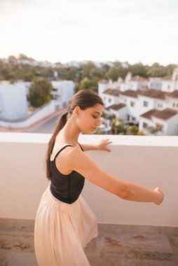 Zarif bir dansçı zarif bir poz veriyor manzaralı bir çatıda, çarpıcı bir günbatımı arka planıyla çerçevelenmiş.