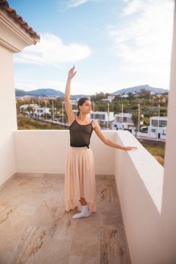 Yetenekli bir dansçı, göz kamaştırıcı bir manzara içeren bir balkonda zarif bir poz verir.