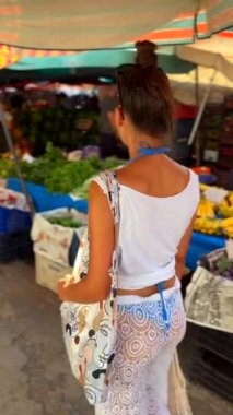 Genç bir kadın açık hava pazarında taze ve bol sebze almaktan zevk alıyor.