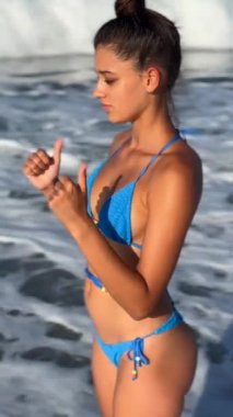 Genç bir kadın şık mavi bir bikiniyle güzel bir plaj gününün tadını çıkarıyor. Yaz havasını ve yaşam tarzını kucaklıyor.