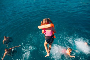 Bir grup mutlu çocuk neşeyle okyanusa sıçrıyor, can yelekleri giyiyor ve neşeli anlarının tadını çıkarıyorlar.