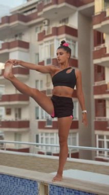 Bir kadın açık havada yoga yapıyor. Dengesini ve gücünü şehir zeminine karşı gösteriyor.