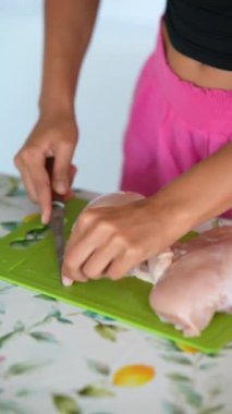 Canlı, dekore edilmiş bir mutfakta yeşil bir kesme tahtasıyla taze tavuk göğsünü ustalıkla dilimleyen biri.
