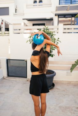 Bir kadın açık havada zarif bir yoga pozu veriyor. Mavi bir egzersiz topuyla güç ve esneklik sergiliyor..