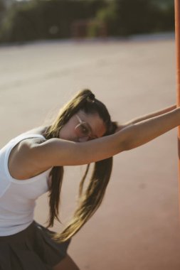 Genç bir kadın aktif olarak açık hava spor tesislerinde dinamik esneme hareketleriyle meşgul.