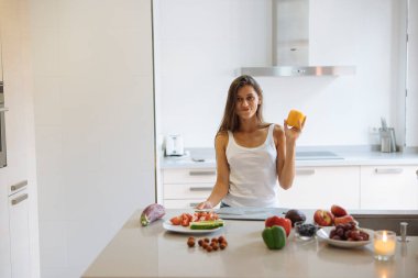 Işıl ışıl yanan bir mutfakta, bir kadın bir dizi taze meyveyle çevrelenmiş lezzetli peyniri neşeyle tutar.