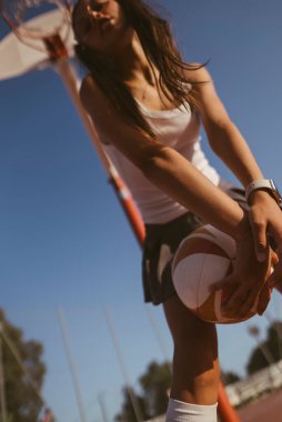 Enerjik ve dinamik bir sahne. Kararlı genç bir bayan basketbolcuyu atış yapmaya hazırlanırken yakalıyor.