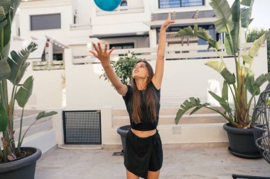 Güneşli bir günün tadını çıkaran genç bir kadın, neşeli bir şekilde açık havada mavi bir topa uzanıyor..