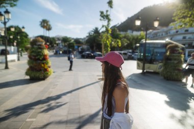 Güzel yeşilliklerle çevrili canlı ve canlı bir kasaba meydanında güneşli bir günün keyfini çıkaran genç bir kadın.