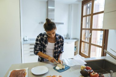 Bir kadın güzel tasarlanmış modern bir mutfak alanında çeşitli taze malzemeleri ustalıkla dilimler.