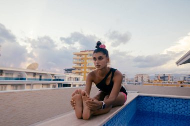 Esnek bir birey güzel bir gün batımında dingin bir havuz kenarında yoga pozu veriyor.