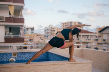 Bir kadın huzur dolu bir havuzun yanında, hem dinginliği hem de zindeliği güzel bir şekilde somutlaştıran sakinleştirici bir yoga pozu veriyor.