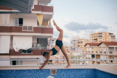 İnanılmaz yetenekli bir akrobat, hem enerji hem de zarafeti yakalayan parıldayan havuzun yanında çarpıcı bir amuda kalkıyor.
