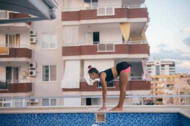 Neşeli bir kız, uzun apartman binaları etrafını sarmışken, kendini parlayan havuza dalmaya hazırlıyor.