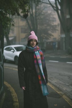 Şık pembe şapkalı ve eşarplı bir kadın şu anda yolun kenarında dikilip manzaraya bakıyor.